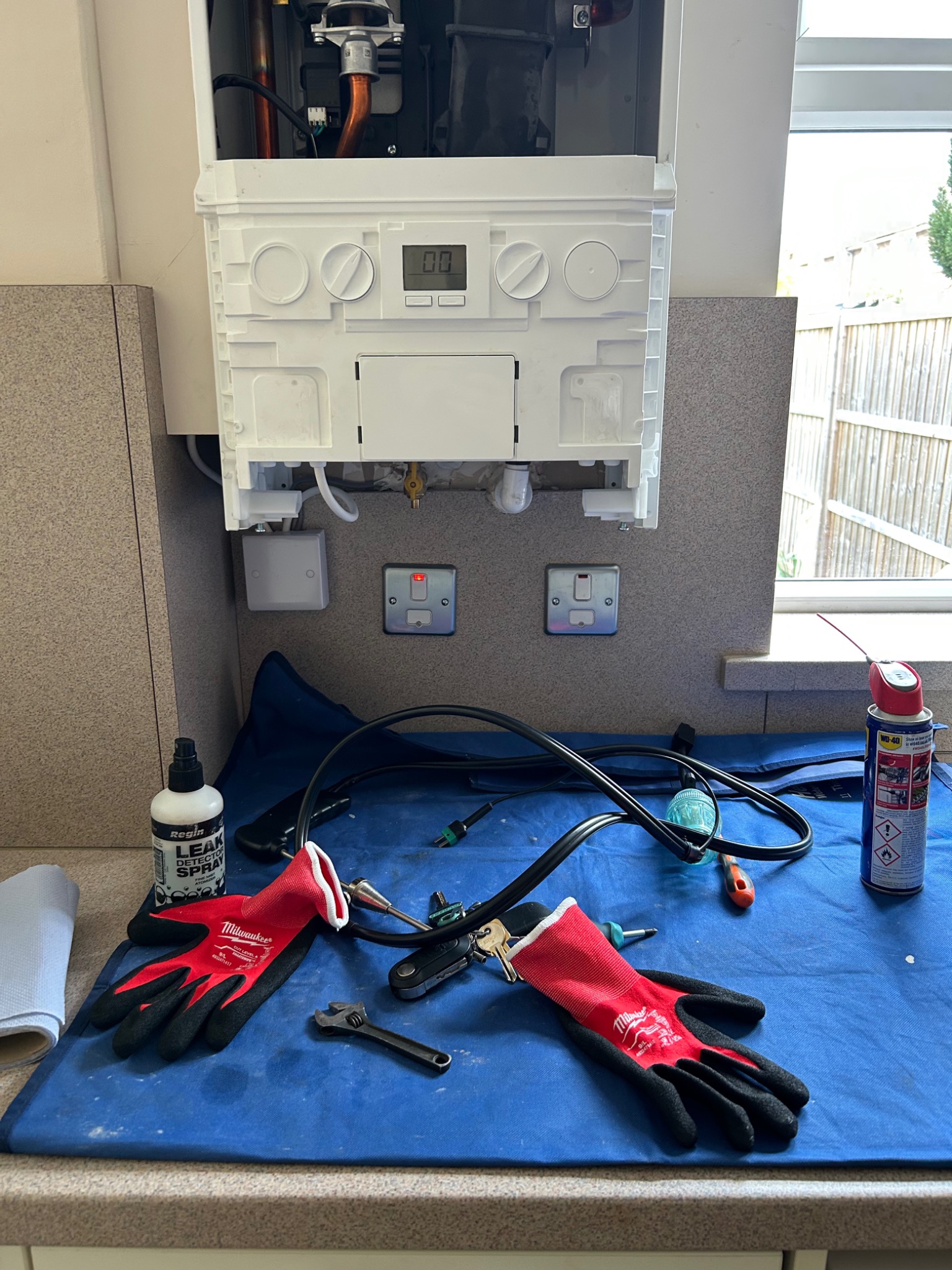 Open gas boiler during servicing, with tools on a blue protective mat.